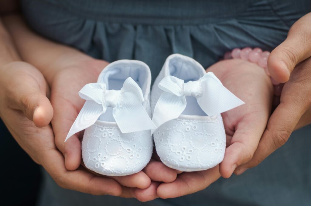 pexels-photo-754953-754953 Close-up photo of hands holding white baby shoes with delicate bows, showcasing love and anticipation.